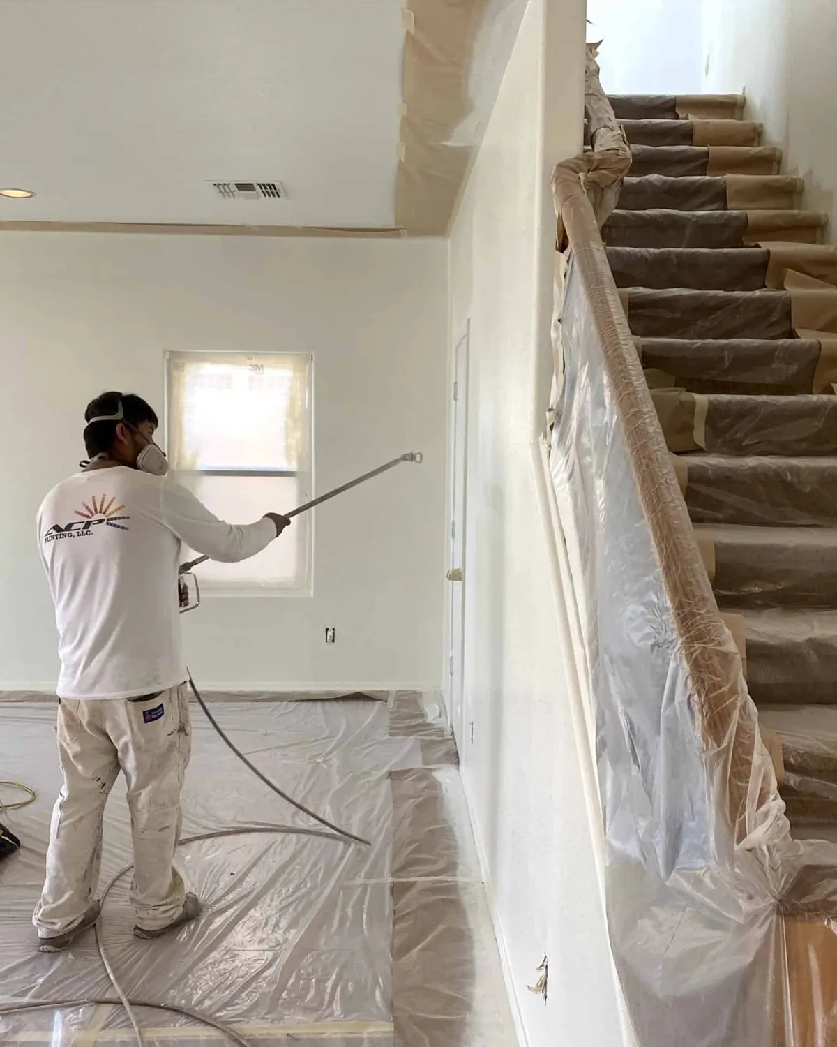 ACP Painting crew member spraying an interior wall with the stairs and railing fully masked