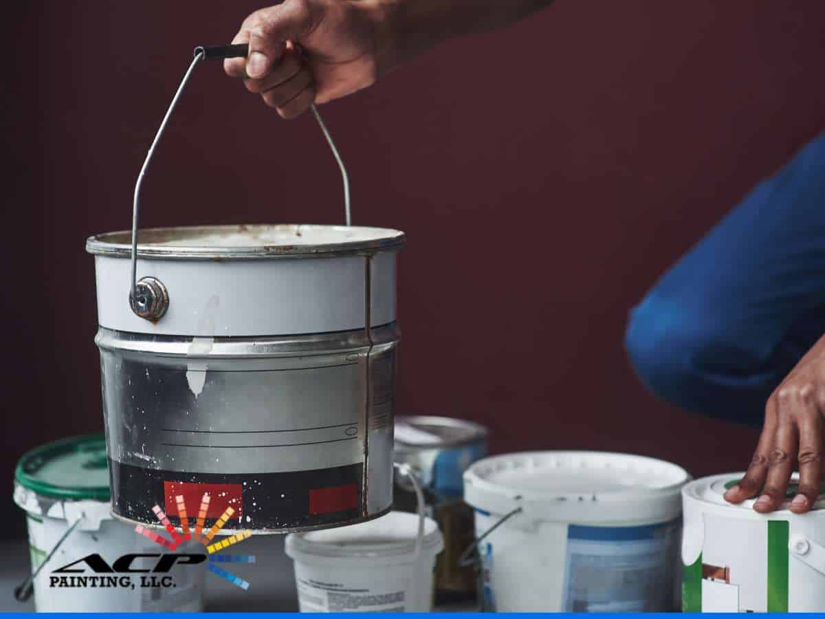 Hand holding bucket of Elastomeric Paint with other paint containers nearby